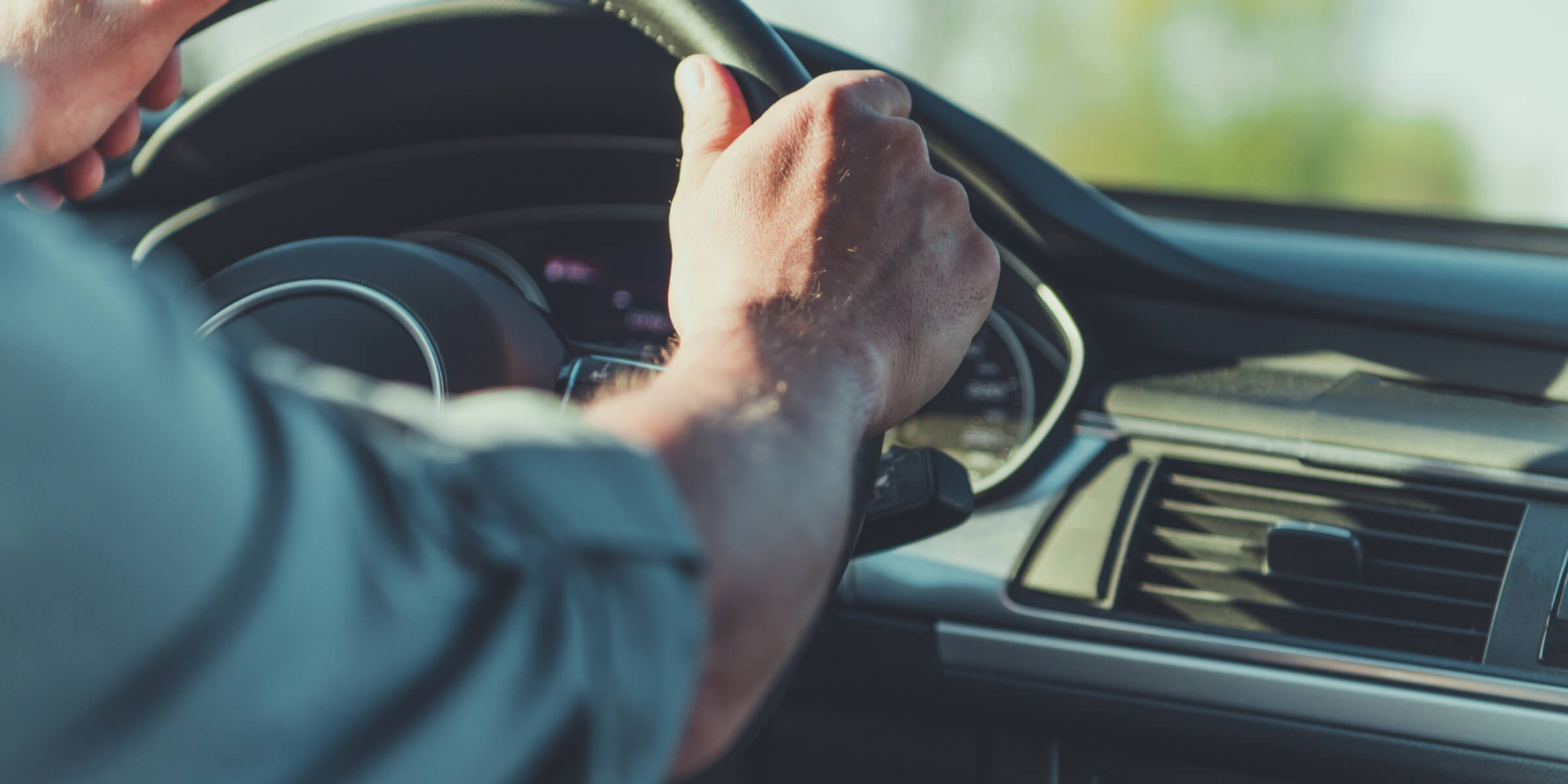 A man is driving a car, hands firmly on the steering wheel, demonstrating concentration and control.